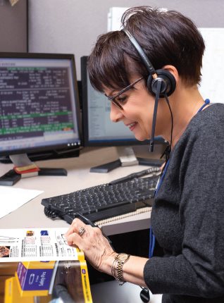 Cleaner's Supply Customer Service Representative References Catalog while on headset at desk by computer